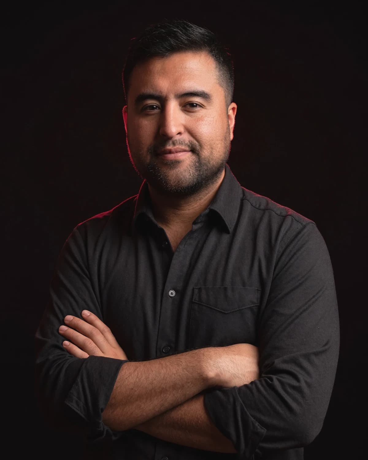 Luis Metzger, arms crossed, lit from one side against a near black ground.